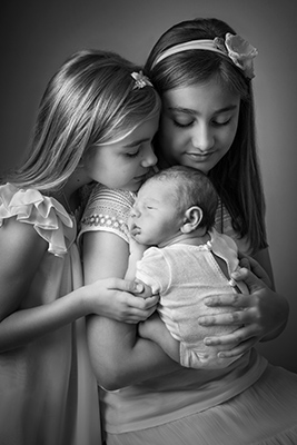 Bébé dans les bras de ses soeurs lors d'une séance photo naissance à Dijon