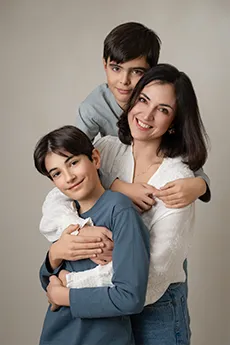 Maman souriante enlacée par ses deux fils sur fond beige, séance photo famille à Dijon
