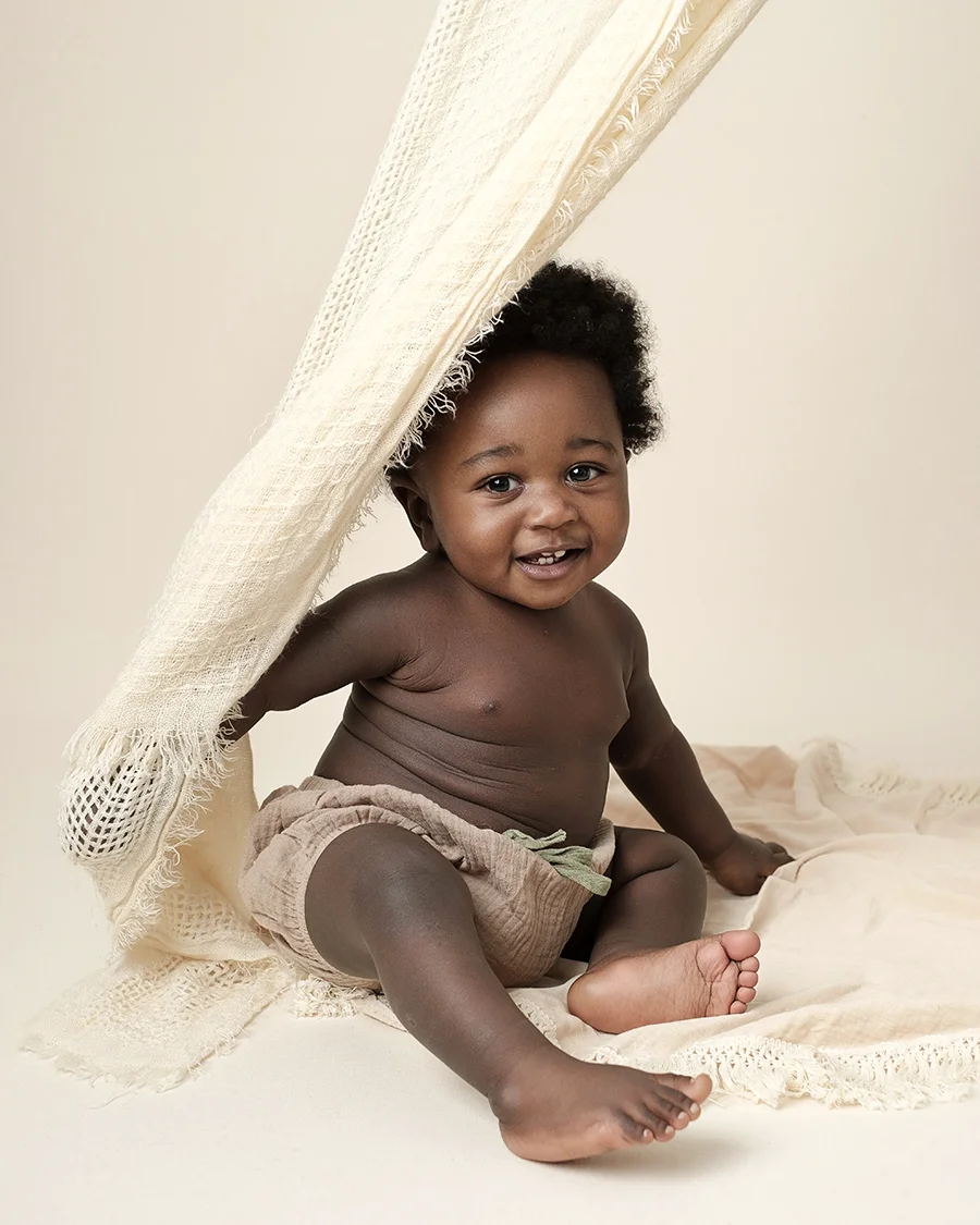 Bébé de 10 mois assis et souriant jouant avec un tissu beige