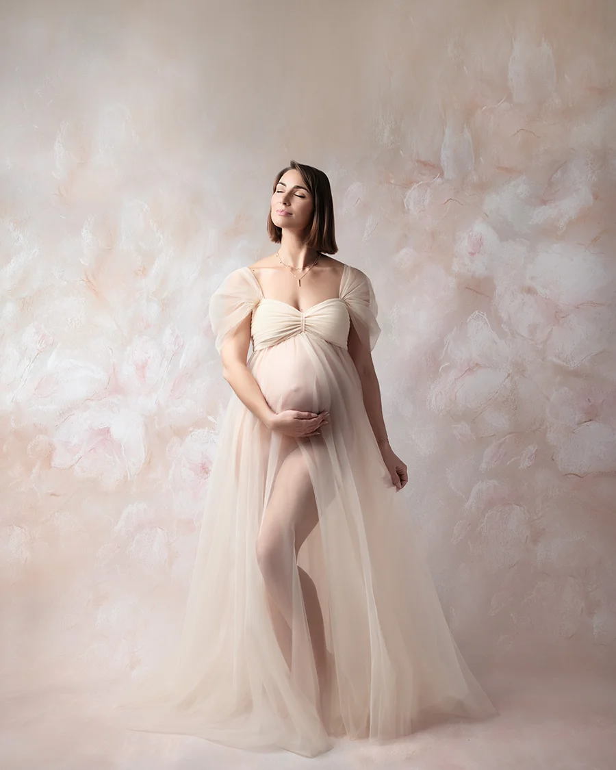 Femme enceinte portant une robe en tulle délicate sur un fond fleuri pastel